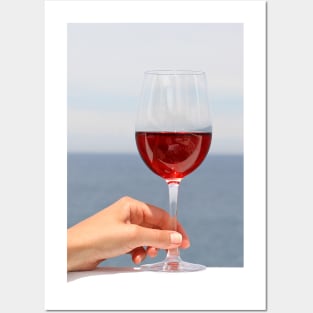 Hand with glass of wine, blue sea in background Posters and Art